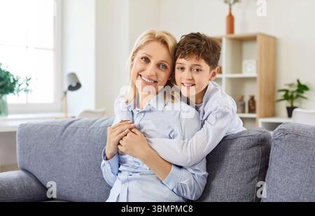 Portrait de mère heureuse et fils assis sur le canapé embrassant ensemble Banque D'Images