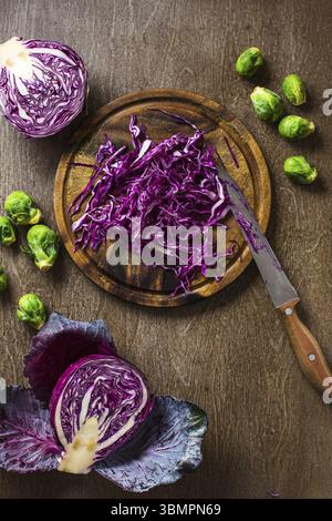 Un choux rouge en tranches et des choux de bruxelles sur fond d'ardoise et de comptoir en bois, sur le plateau avec un couteau Banque D'Images