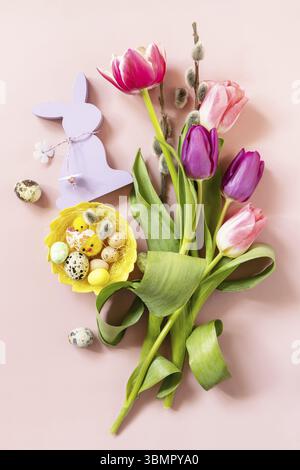 Tulipes roses et violettes avec des œufs de caille colorés dans un nid sur fond rose. Concept de vacances de printemps et de Pâques. Vue de dessus à plat Banque D'Images