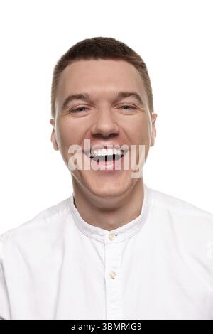 Charmanter huebscher junger Mann im weissen Hemd schneidet Grimassen, waehrend er isoliert auf einem weissen Hintergrund steht Banque D'Images
