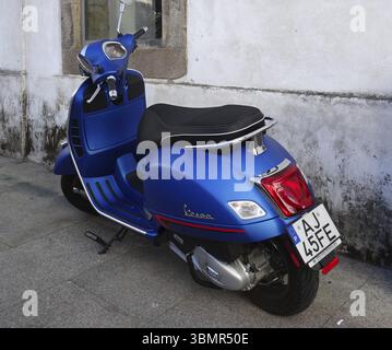 Scooter Vespa bleu moderne garé sur un trottoir près d'un vieux mur blanc, mettant en valeur son design élégant et son attrait urbain Banque D'Images