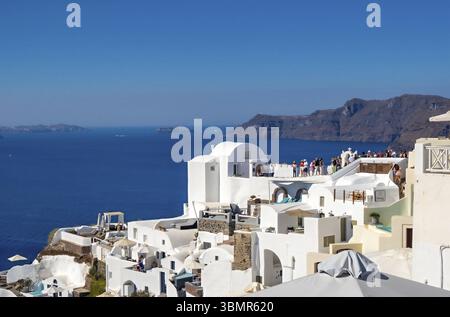 Touristes appréciant la vue panoramique sur la mer Égée et la caldeira volcanique depuis un toit à Oia, Santorin Banque D'Images