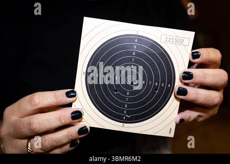 Landkreis Osnabrück, Deutschland 25. Juni 2025 : Im Bild : Zwei Hände mit dunklem Nagellack halten eine klassische Papierscheibe, die nach einer Schussserie im 50-Meter-Kleinkaliber KK-Schießen verwendet wurde. Auf der Scheibe sind mehrere Trefferlöcher sichtbar, die das Schießergebnis einer Athletin oder eines Athleten dokumentieren. Die Ringeinteilung der Scheibe, von außen nach innen nummeriert, dient der Bewertung der Präzision. Die Seriennummer 121502 ist oben rechts auf der Scheibe vermerkt. Dieses Bild zeigt das unmittelbare Ergebnis des Präzisionsschießens und die greifbaren Resultate de Banque D'Images