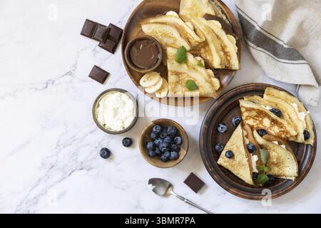 Fête du Pancake, petit déjeuner sain. Délicieuses crêpes maison au caramel au chocolat, aux bananes et aux myrtilles et à la ricotta sur un plan d'examen en marbre Banque D'Images