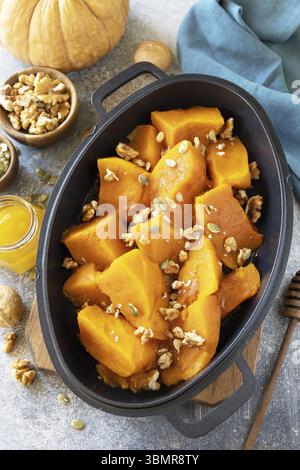 Dessert sain ou déjeuner végétalien. Citrouille cuite au four. Délicieuse citrouille sucrée cuite au four avec des noix, des graines de citrouille et du miel sur fond de pierre grise Banque D'Images
