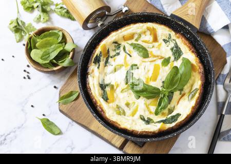 Omelette aux épinards et au fromage. Frittata faite d'œufs, paprika et épinards dans une poêle sur un comptoir en marbre. Copier l'espace Banque D'Images