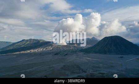 Un panache de fumée volcanique s'élève du mont bromo dans l'est de Java en Indonésie, créant une scène dramatique contre le paysage accidenté et la vaste caldeira ci-dessous. Banque D'Images