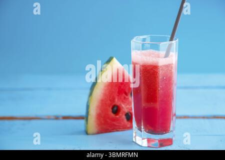 Un morceau de pastèque et smoothie, jus de pastèque fraîchement pressé dans un verre transparent sur un fond en bois bleu Banque D'Images