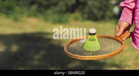 Main féminine tenant le volant de badminton jaune néon et la raquette en bois à l'extérieur. Copie de l'espace de mise au point sélective douce sur les volants. Remise en forme alternative Banque D'Images