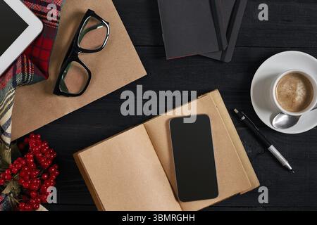Vue ci-dessus du smartphone avec ordinateur portable et tasse de café latte sur fond noir en bois. Encore la vie. Copier l'espace. Pose à plat. Vue de dessus Banque D'Images