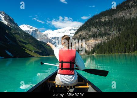 Femme en canoë pointant vers des montagnes enneigées par temps clair. Banque D'Images
