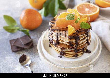 Célébration de la journée des crêpes, petit déjeuner sain. Délicieuses crêpes de bananes américaines maison avec chocolat et orange rouge sur fond de pierre grise Banque D'Images