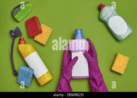 Détergents professionnels et accessoires de nettoyage, tels que : femmes mains dans un caoutchouc violet gants tiennent un nettoyant pour la vaisselle avec une étiquette vide Banque D'Images