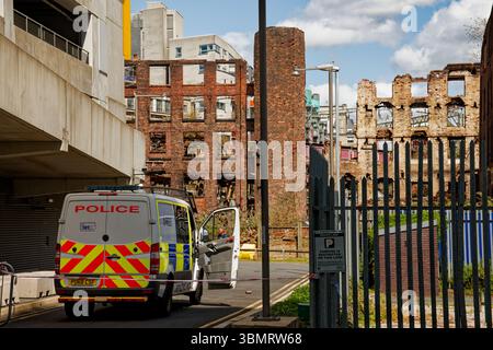 Une camionnette de la police garde le cordon de sécurité autour des ruines dangereuses de l'usine Hotspur Press après un incendie désastreux en juin 2025 à Manchester. Banque D'Images