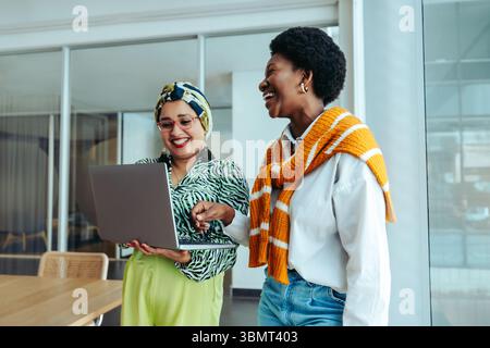 Des collègues sympathiques profitent d'une collaboration animée dans un bureau d'agence moderne, partageant des idées sur un ordinateur portable. Mettre en avant le travail d'équipe et la communication Banque D'Images