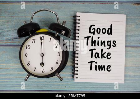 Les bonnes choses prennent du temps texte écrit sur bloc-notes avec réveil sur fond en bois Banque D'Images