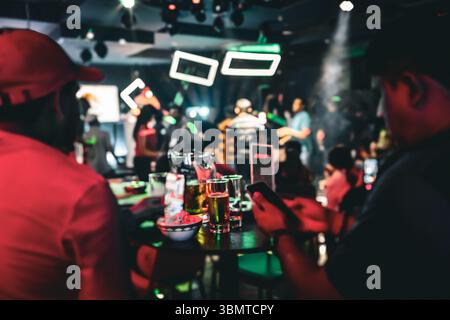 Dans un bar très éclairé avec des lumières violettes et roses, les gens s'engagent dans des conversations et apprécient la bière Banque D'Images