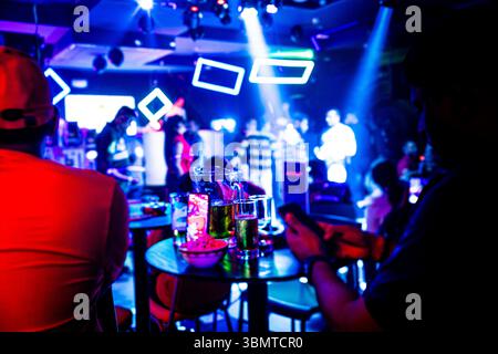 Dans un bar très éclairé avec des lumières violettes et roses, les gens s'engagent dans des conversations et apprécient la bière Banque D'Images