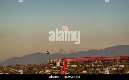 Beau paysage de crépuscule montrant la lune au-dessus d'une ville et des Alpes Banque D'Images