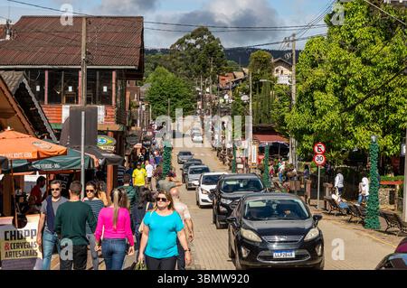 Avenue pavée bondée Monte Verde, animée par les piétons, la circulation automobile, beaucoup de magasins et des arbres sous un ciel partiellement nuageux. Banque D'Images