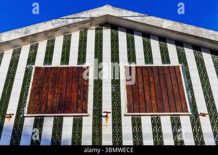 Une façade de bâtiment saisissante présente un motif audacieux de carreaux rayés verts et blancs avec deux couvre-fenêtres en bois vieilli, mettant en valeur la côte unique Banque D'Images