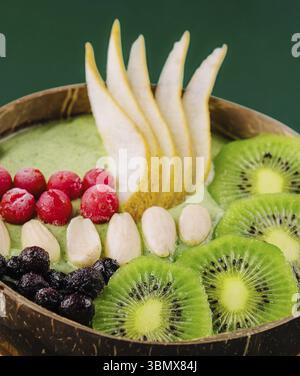 Nature morte, bol à smoothie vert avec noix, kiwi, poire, baie et granola Banque D'Images