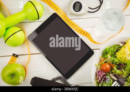 La tablette noire est montrée dans un design plat sur une table en bois, avec haltères, chronomètre, saladier Banque D'Images