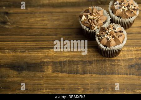 Trois cupcakes au chocolat sont montrés dans un design plat sur une table en bois, espace de copie Banque D'Images