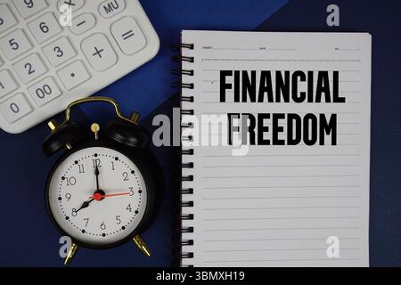 Financial Freedom texte écrit sur bloc-notes avec calculatrice et réveil sur fond bleu marine Banque D'Images