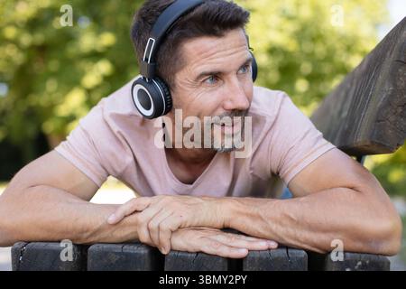 homme assis sur un banc dans le parc écoutant de la musique Banque D'Images