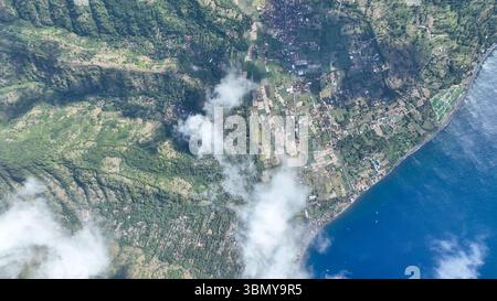 Une vue imprenable de haut en bas révèle le paysage luxuriant et la côte du village d'Amed où les rizières vertes rencontrent la mer d'un bleu profond. Les nuages dérivent Banque D'Images