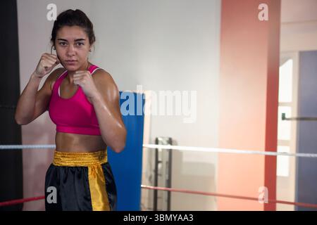 Athlète féminine debout dans un ring de boxe levant les poings portant un soutien-gorge de sport rose short noir Banque D'Images