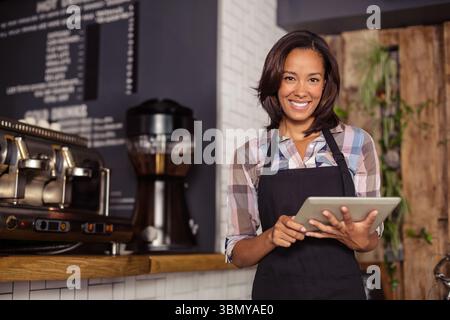 Femme afro-américaine tenant la tablette et souriant au comptoir du café avec machine à expresso, espace de copie Banque D'Images