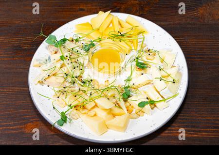 Un plateau de fromages magnifiquement arrangé présente différents types de fromages, arrosés de miel et garnis d'herbes fraîches, le tout sur un t en bois rustique Banque D'Images