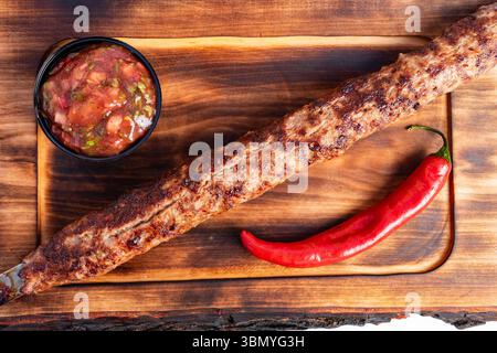 Kebab grillé servi sur une planche de bois avec Chili et salsa dans un éclairage vif Banque D'Images