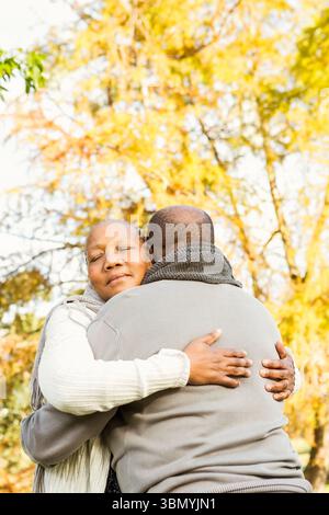 Couple senior afro-américain embrassant et portant des foulards gris dans un parc verdoyant pendant l'automne Banque D'Images