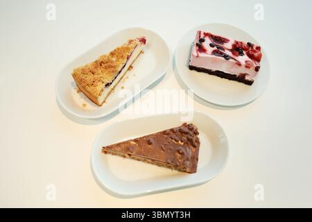 Plan de haut en bas de trois gâteaux différents sur des assiettes blanches : cheesecake aux baies, tranche de noisette au chocolat et une barre de mousse crémeuse aux baies Banque D'Images