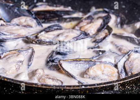 Les moules en coquille dans une sauce crémeuse sont cuites dans une poêle. Gros plan. Fond texturé. Macrophotographie. Photo de haute qualité Banque D'Images