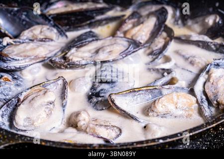 Les moules en coquille dans une sauce crémeuse sont cuites dans une poêle. Gros plan. Fond texturé. Macrophotographie. Photo de haute qualité Banque D'Images