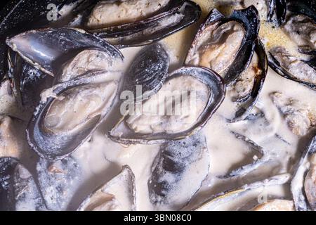 Les moules en coquille dans une sauce crémeuse sont cuites dans une poêle. Gros plan. Fond texturé. Macrophotographie. Photo de haute qualité Banque D'Images
