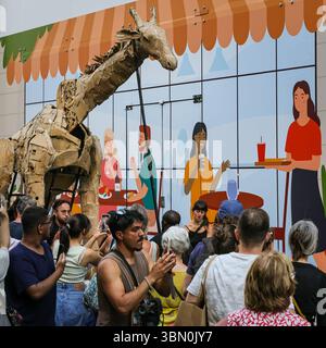 Londres, Royaume-Uni. 29 juin 2025. Les troupeaux trottent le long des boutiques et se mêlent aux spectateurs curieux. LES marionnettes d'animaux géants des TROUPEAUX rencontrent une intervention de danse des danseurs de Sadler's Wells qui tentent d'arrêter LES TROUPEAUX alors qu'ils voyagent de Westfield Stratford à Sadler's Wells East où ils jouent dans une finale. LES TROUPEAUX sont l'art public et l'action climatique. D’avril à août 2025, les animaux marionnettes grandeur nature parcourent un itinéraire de 20 000 km entre le bassin du Congo et le cercle arctique, symbolisant leur fuite de la catastrophe climatique avec des arrêts dans de nombreuses villes et pays, à Londres du 27 au 29 juillet. Banque D'Images