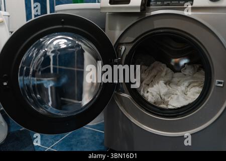 Machine à laver moderne avec porte ouverte, tambour de présentation rempli de serviettes blanches moelleuses, prêt pour le cycle de lavage dans un environnement de salle de bains moderne, Banque D'Images