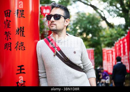Jeune homme appuyé contre la porte torii rouge au Japon, voyageur urbain élégant Banque D'Images