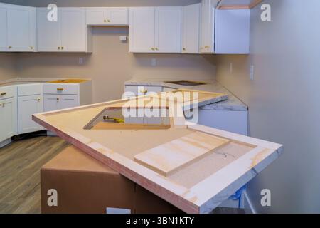 Les ouvriers de la construction se préparent à installer un comptoir en marbre dans une cuisine contemporaine avec des armoires blanches. Banque D'Images