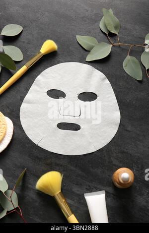 Masque de drap facial avec différents produits cosmétiques et eucalyptus sur fond noir Banque D'Images