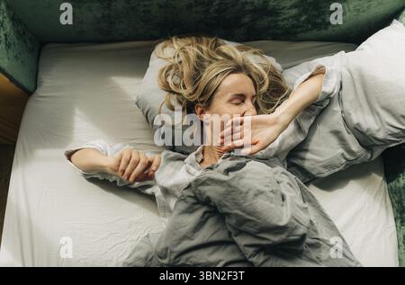 Eine Frau streckt sich nach dem Aufwachen und gaehnt im Bett liegend am Morgen Banque D'Images