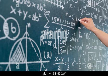 Gros plan d'une main écrivant des formules mathématiques compliquées et des équations scientifiques sur un tableau noir. Image idéale pour l'éducation, l'école, la science, le journal Banque D'Images