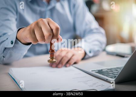 gros plan d'une main apposant un cachet légal à un contrat dans un bureau, signifiant l'approbation finale et l'authentification d'un document d'affaires important Banque D'Images