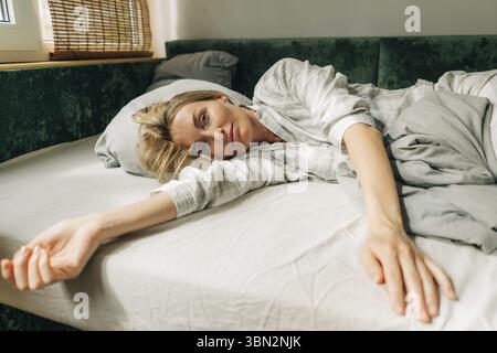 Belle femme en pyjama se trouve sur le lit le matin Banque D'Images