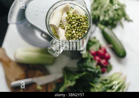Sur la table se trouve un mélangeur rempli de légumes verts, de légumes et de grains germés de purée. Préparer un smoothie de petit déjeuner sain vert. Mode de vie sain et n Banque D'Images